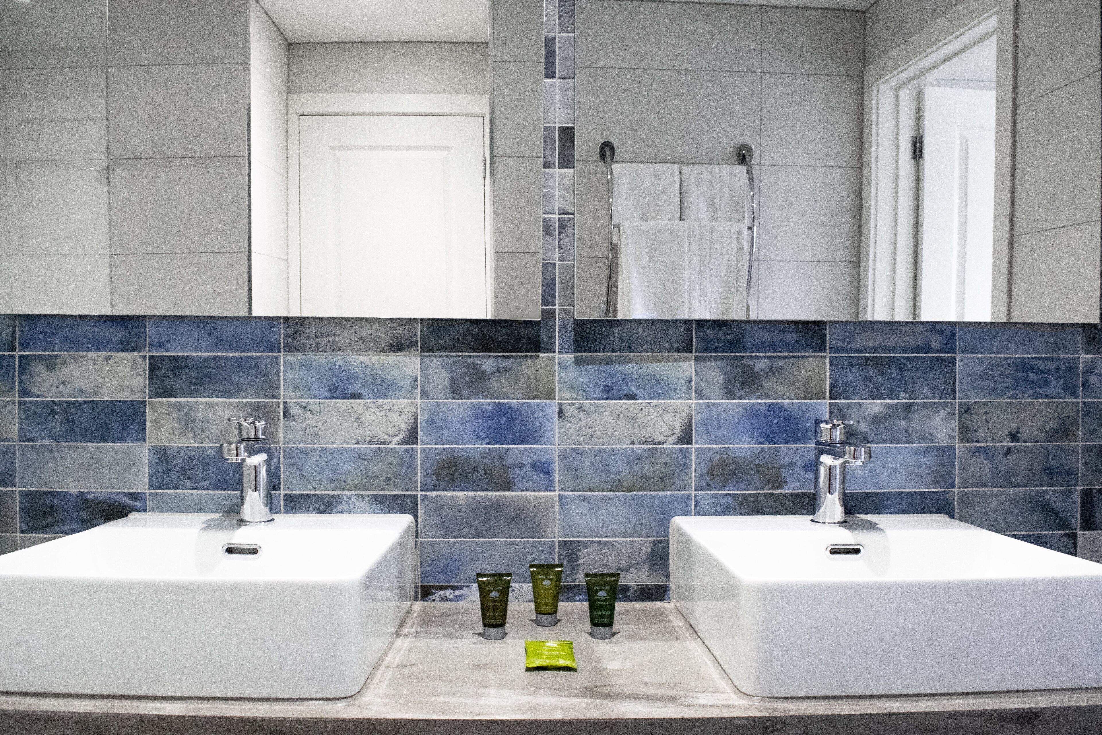 Casa de banho com duas pias, um espelho e painel de azulejos.