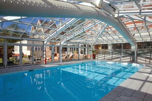 A swimming pool with a glass ceiling, surrounded by outdoor seating and a view of buildings. - Bournemouth West Cliff Hotel & Spa (Bournemouth)