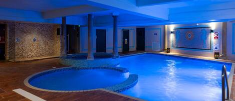 Una piscina interior con pared de azulejos y diseño en mosaico, suelo de madera y señal de profundidad de la piscina.