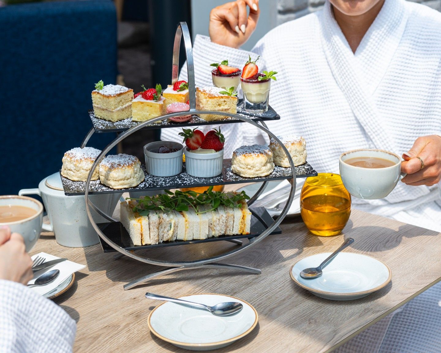 A three-tiered dessert tray with various pastries and a cup of coffee on a table.