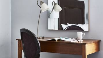 A hotel room with a wooden desk, a chair, a large mirror, and framed pictures on the wall.