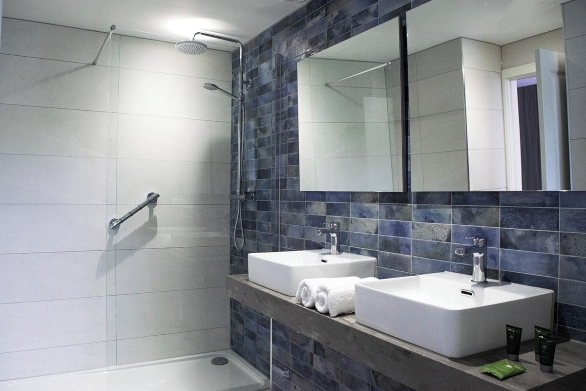 A modern bathroom with two sinks, a shower, and a large mirror.