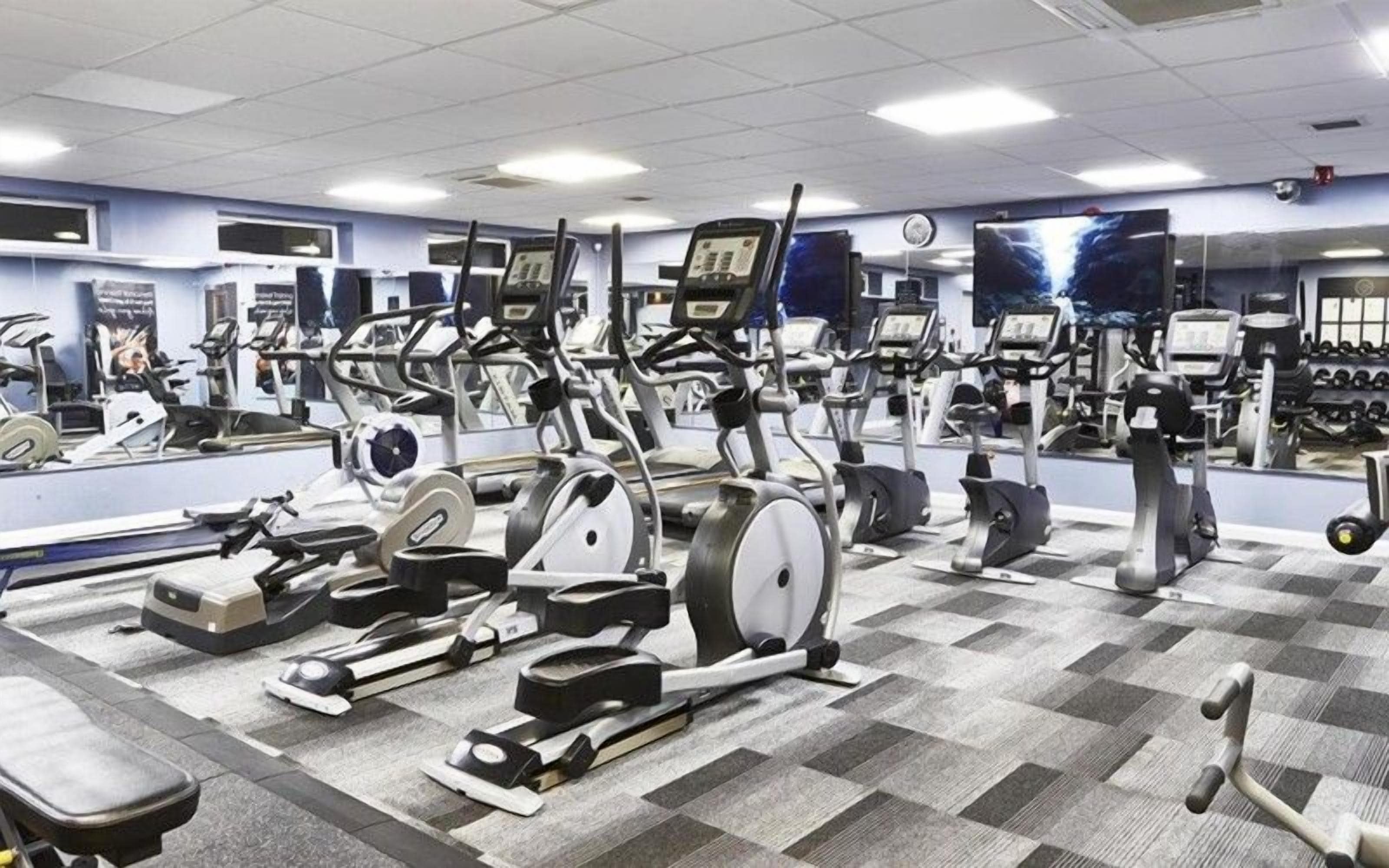 A gym with multiple exercise machines, mirrors, and a checkered floor.