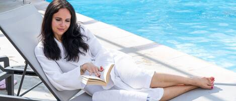 Una persona recostada junto a una tumbona en la piscina, leyendo un libro.