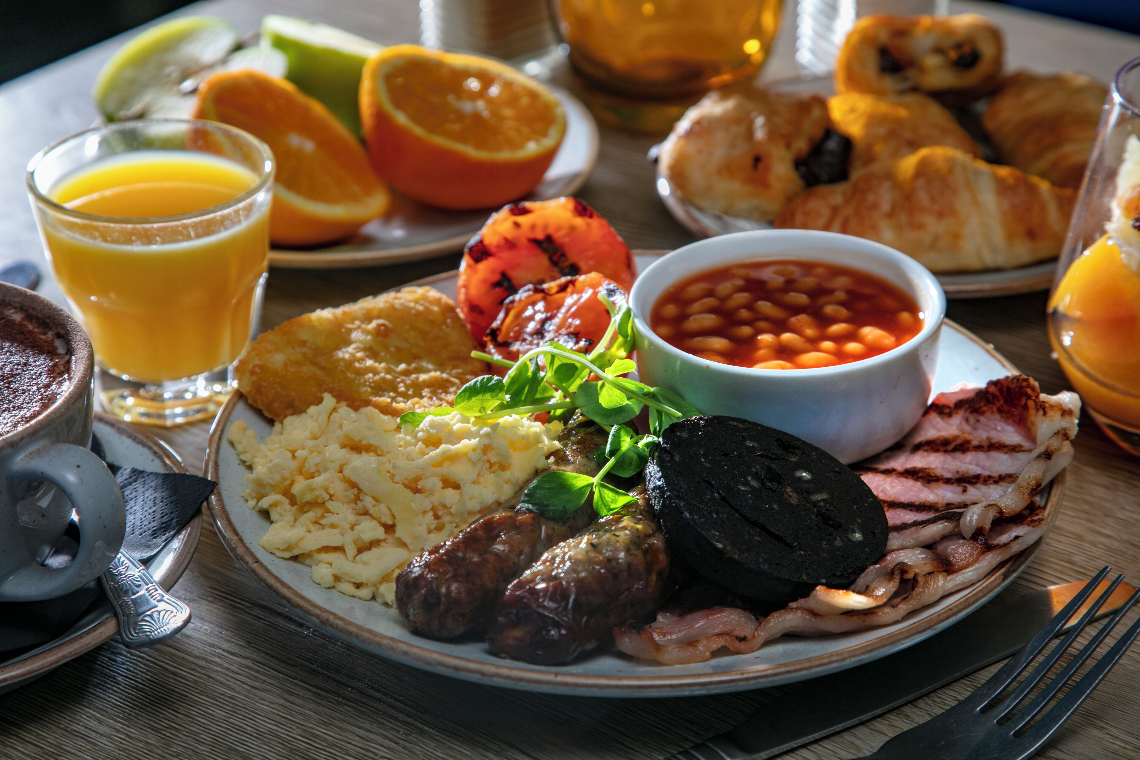 A breakfast plate with eggs, sausages, bacon, beans, and a grilled tomato.