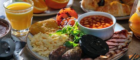 A breakfast plate with eggs, sausages, bacon, beans, and a grilled tomato.