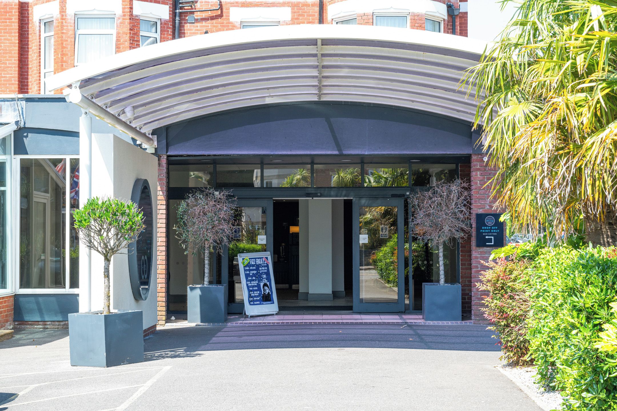 A hotel entrance with a curved canopy, a signboard, and potted plants.