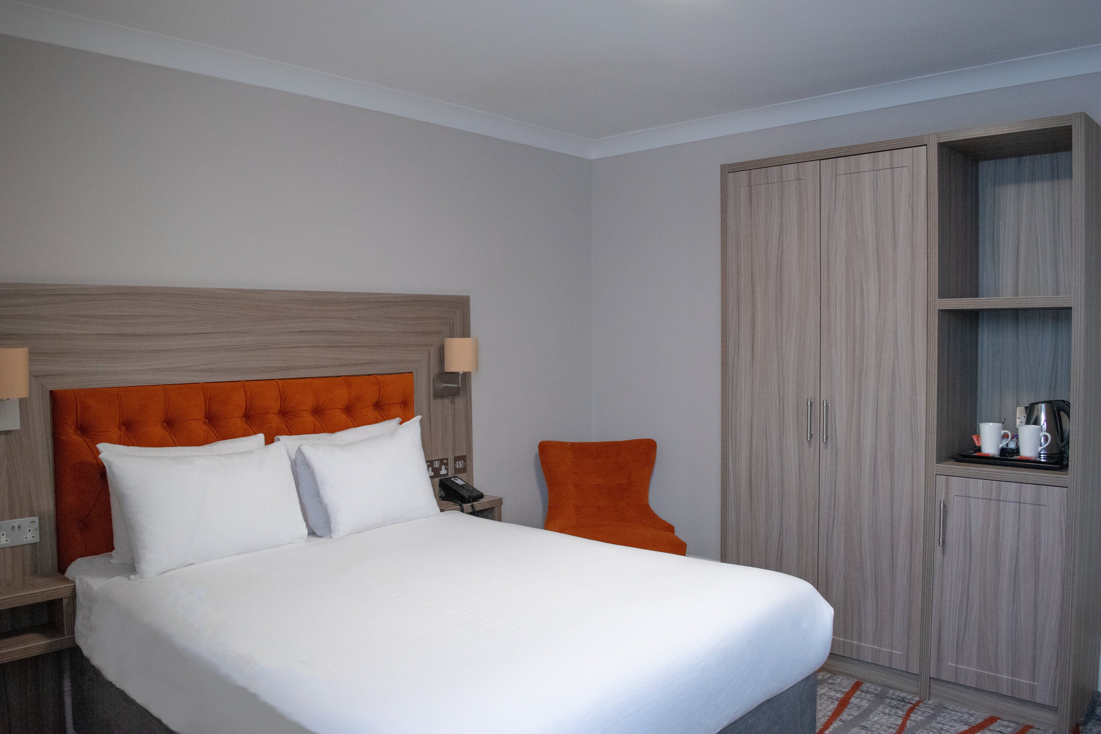 A hotel room with a large bed, a wooden wardrobe, and a small table with a telephone and cups.