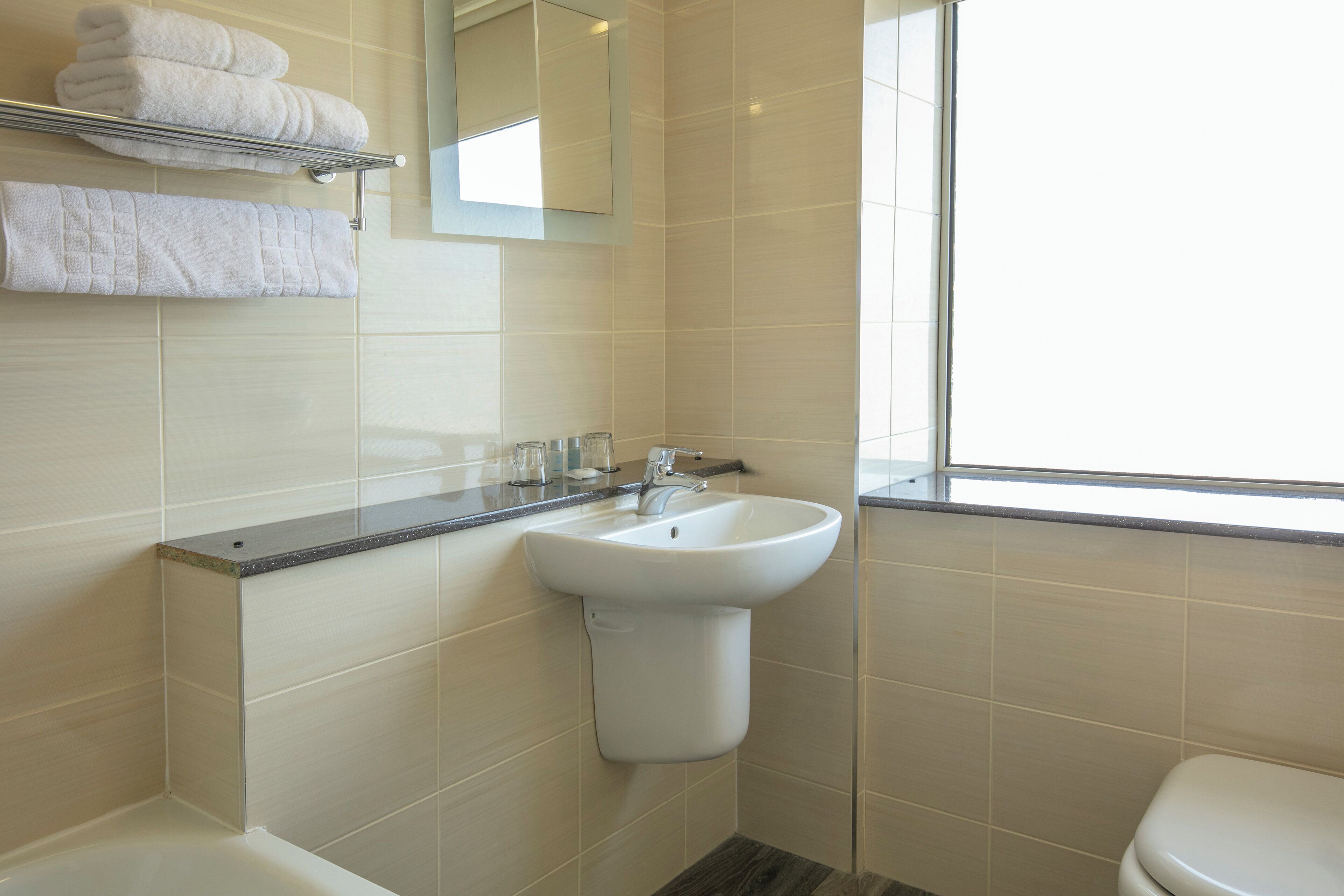 Un bany amb un lavabo blanc, un mirall i una finestra.