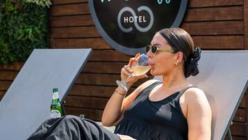 A person relaxing on a lounge chair with a bottle of Peroni beer and a glass of white wine, with a sign for West Cliff Hotel in the background.