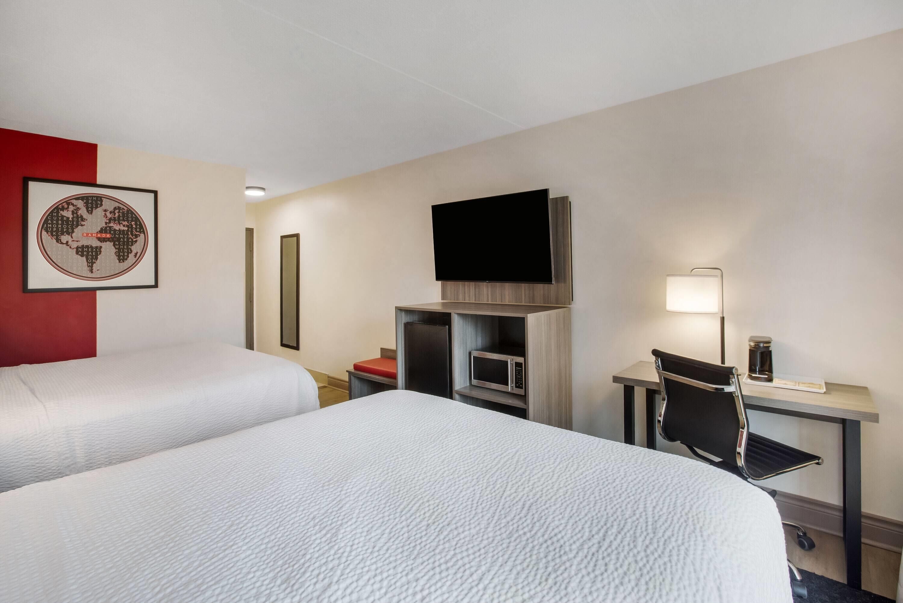 A hotel room with two beds, a TV, a desk with a chair, a lamp, and a microwave.