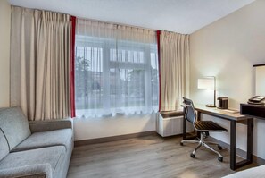 Une chambre d’hôtel équipée d’un canapé, d’un bureau avec une chaise, d’une lampe et d’un climatiseur.