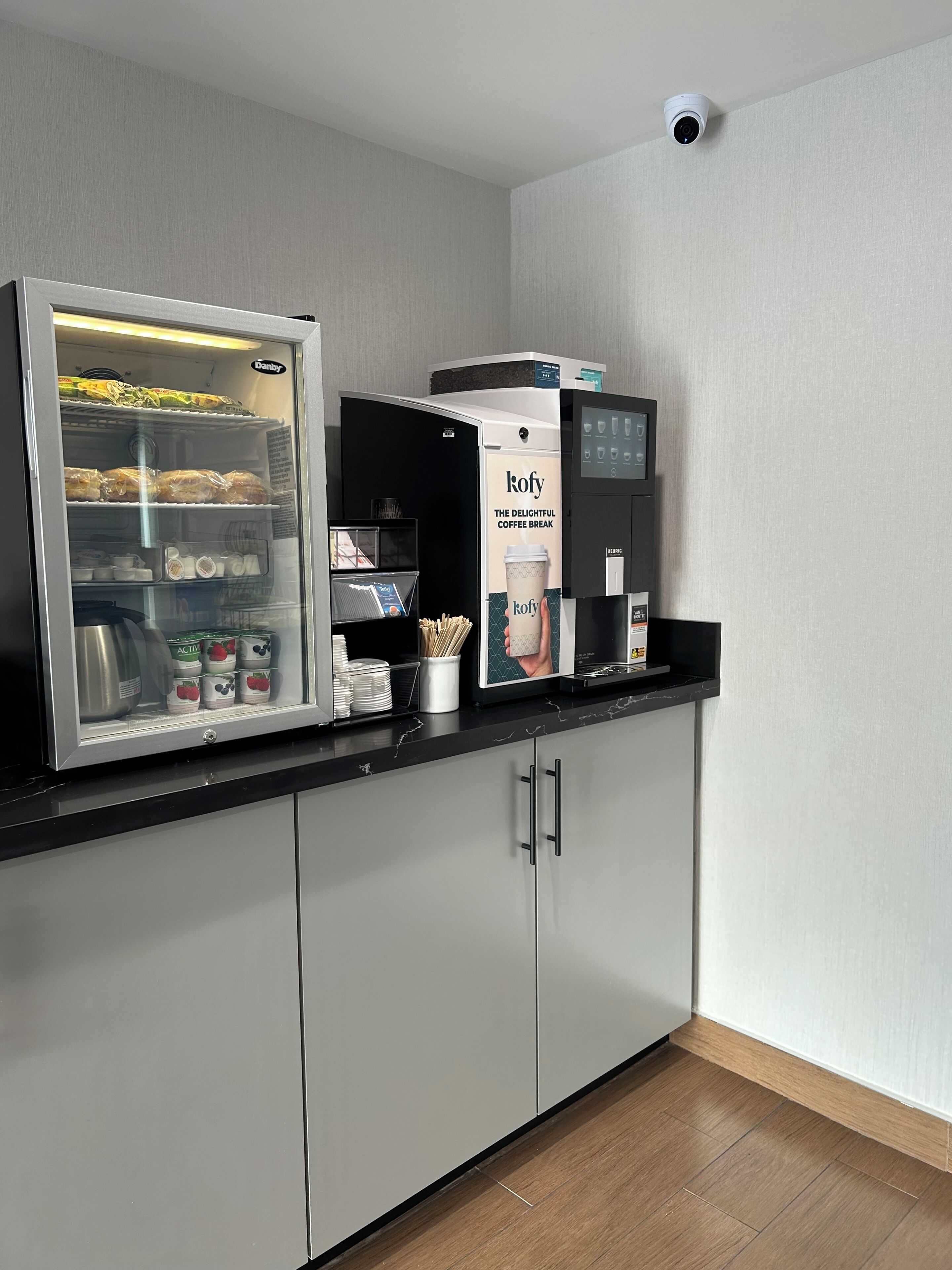 Una kitchenette con refrigerador, cafetera y exhibición de productos de café.