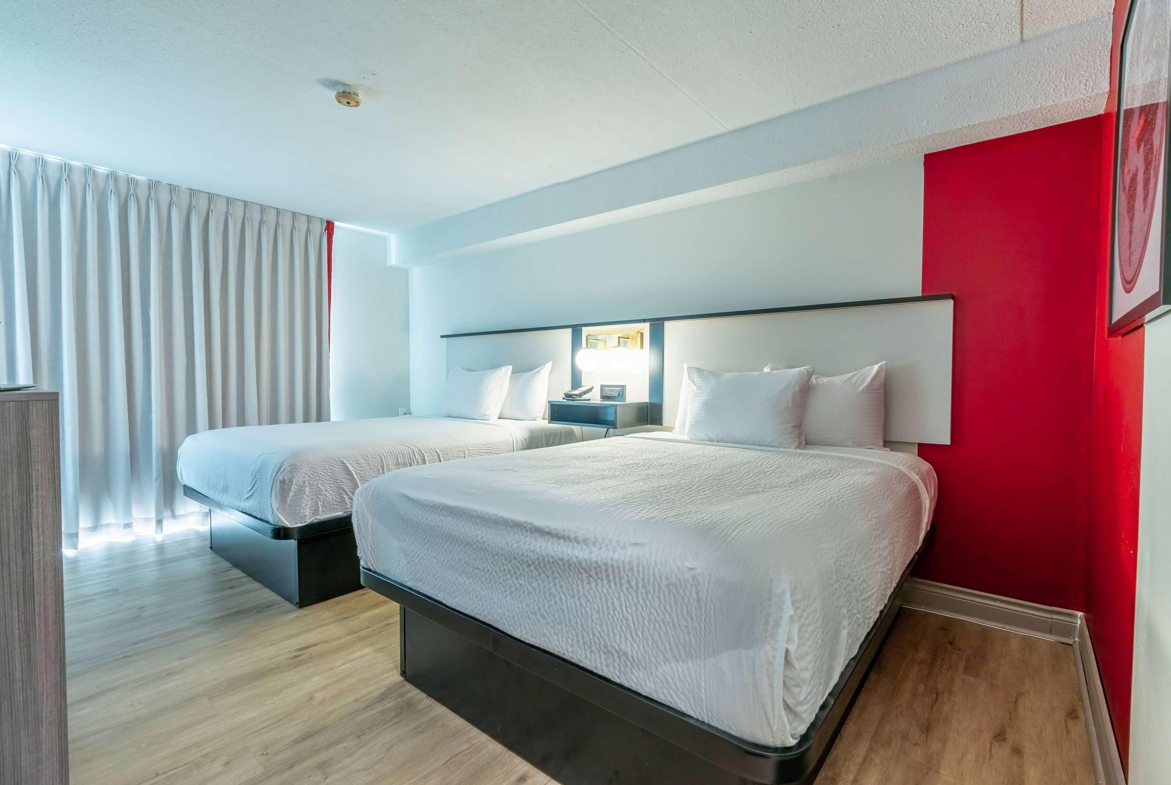 A hotel room with two beds, a nightstand, and a red accent wall.