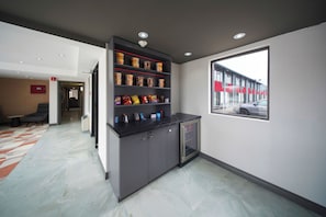 A modern hotel lobby with a marble floor, a dark reception desk with snack dispensers, and a view of a red building outside. - Ramada by Wyndham Kingston (Kingston)