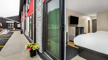 Habitación de hotel con una cama grande, televisión y puerta corrediza de vidrio que da a un balcón con flores.
