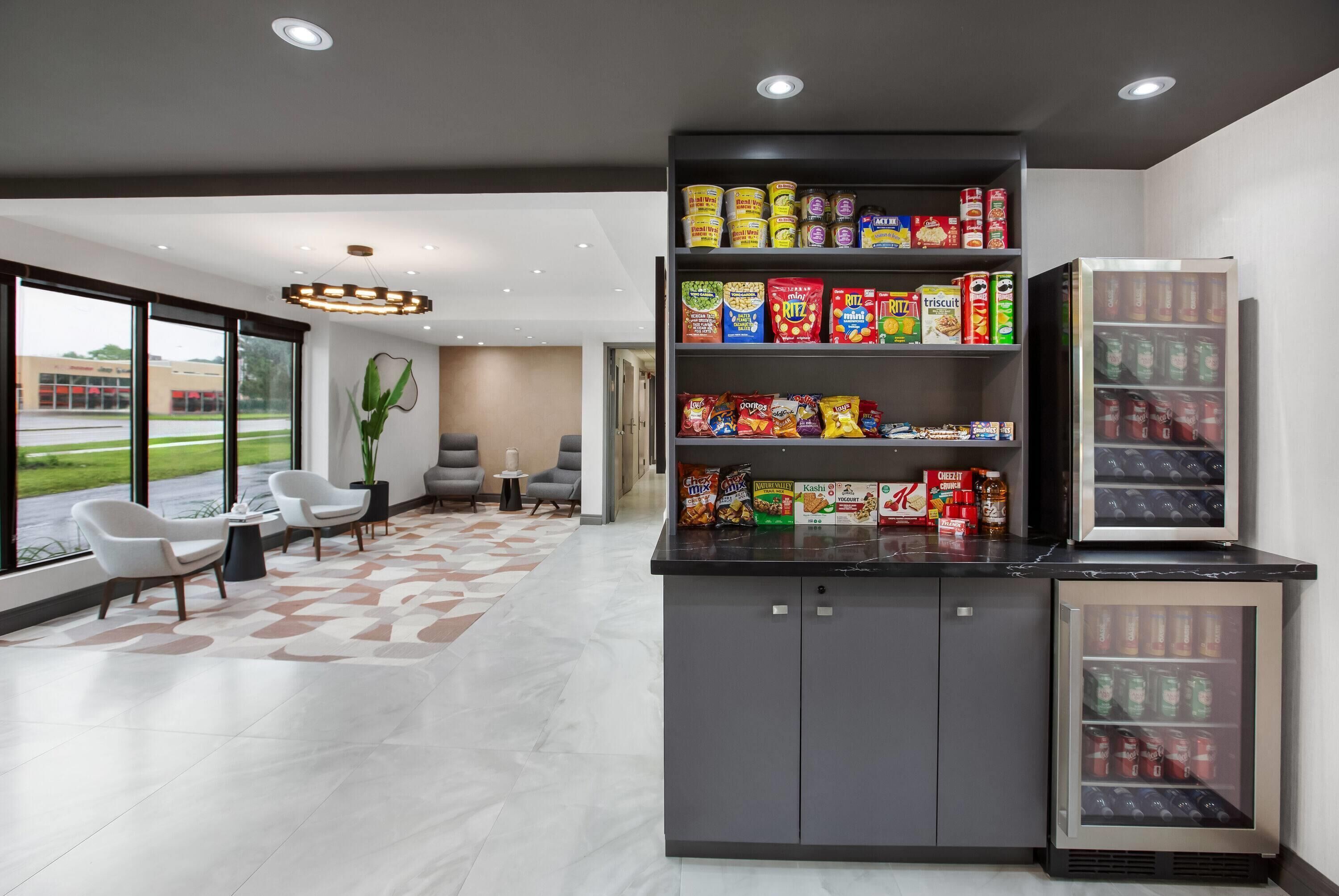 A modern lobby with a seating area, a snack bar with various food items, and a refrigerator.