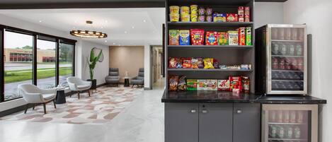 A modern lobby with a seating area, a snack bar with various food items, and a refrigerator.