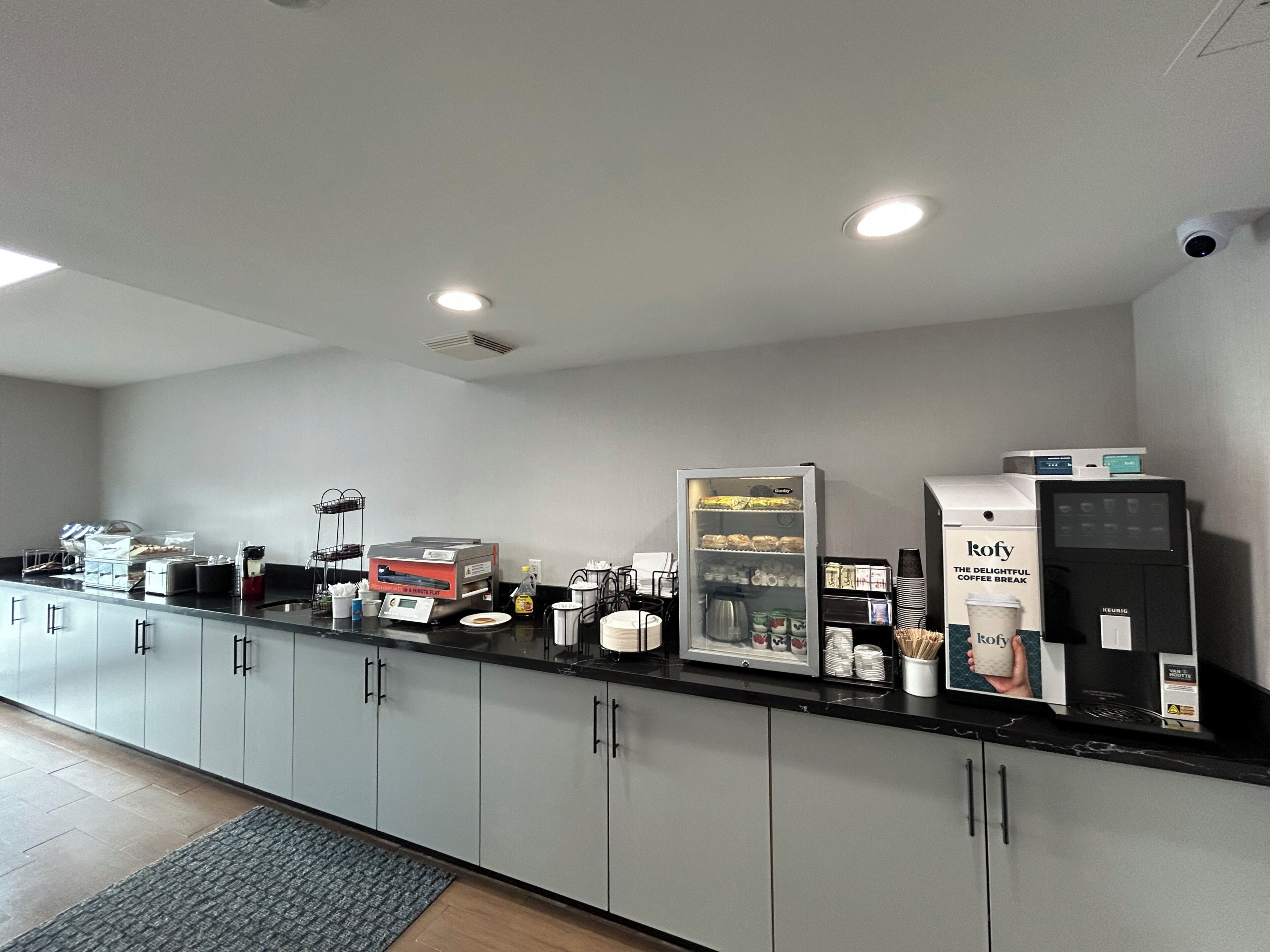 A modern coffee station with a coffee machine, a refrigerator, and a Keurig coffee maker.