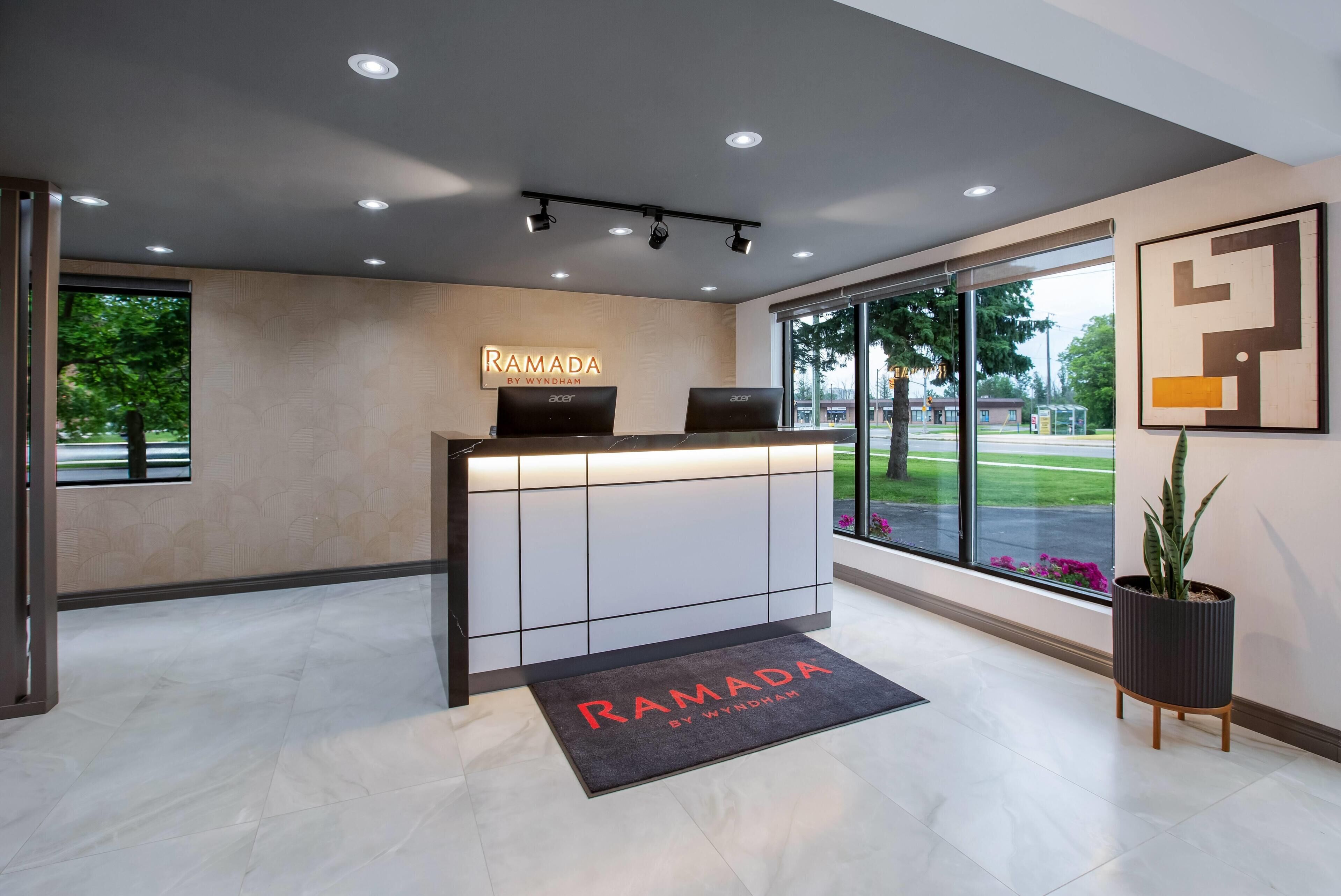 A reception desk with a sign reading 'RAMADA BY WYNDHAM' and two laptops on it.