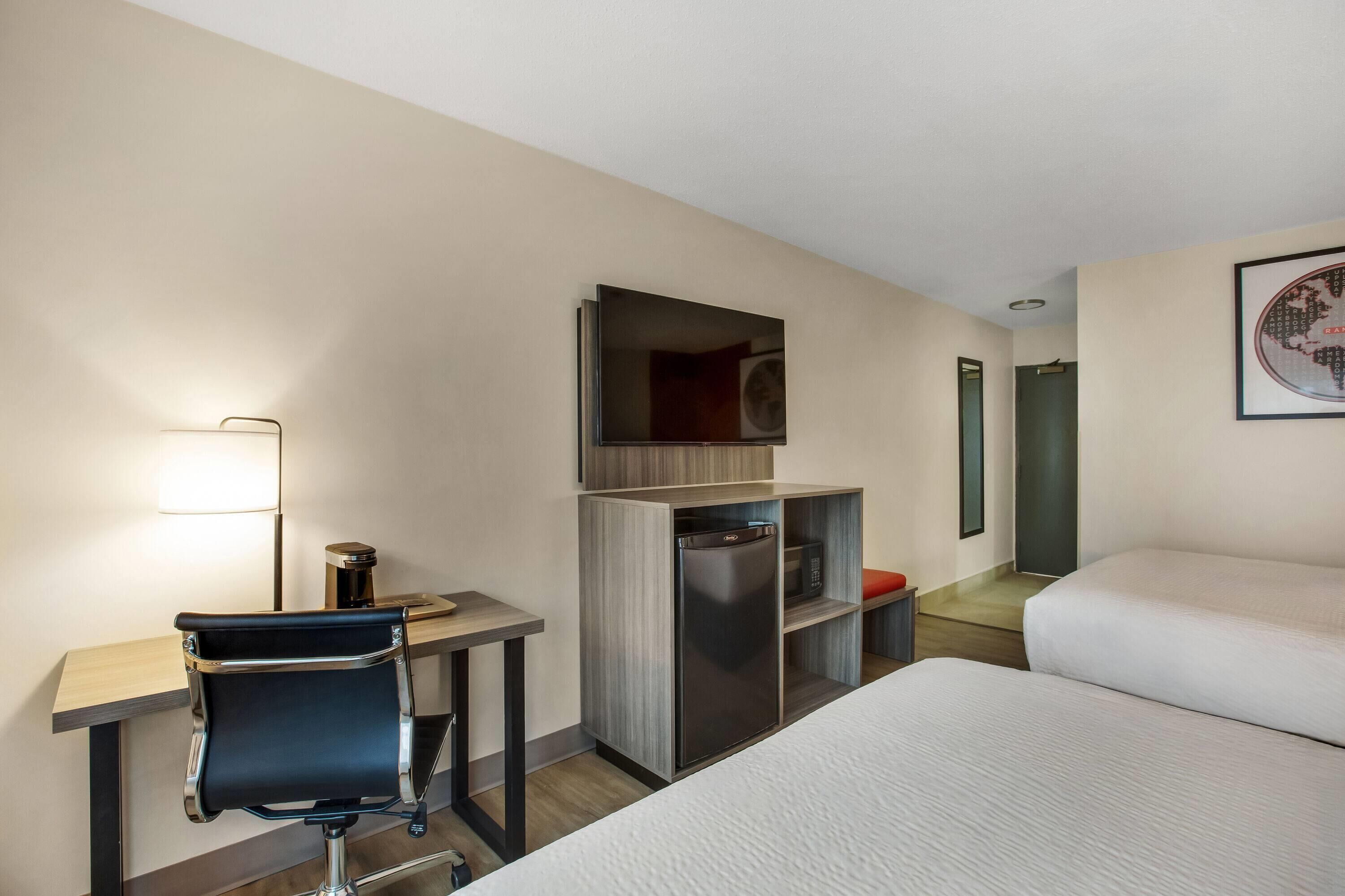 Habitación de hotel con cama, escritorio y silla, refrigerador, microondas, lámpara y un cuadro en la pared.