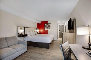 A hotel room with a bed, a sofa, a desk, a TV, and a red accent wall.