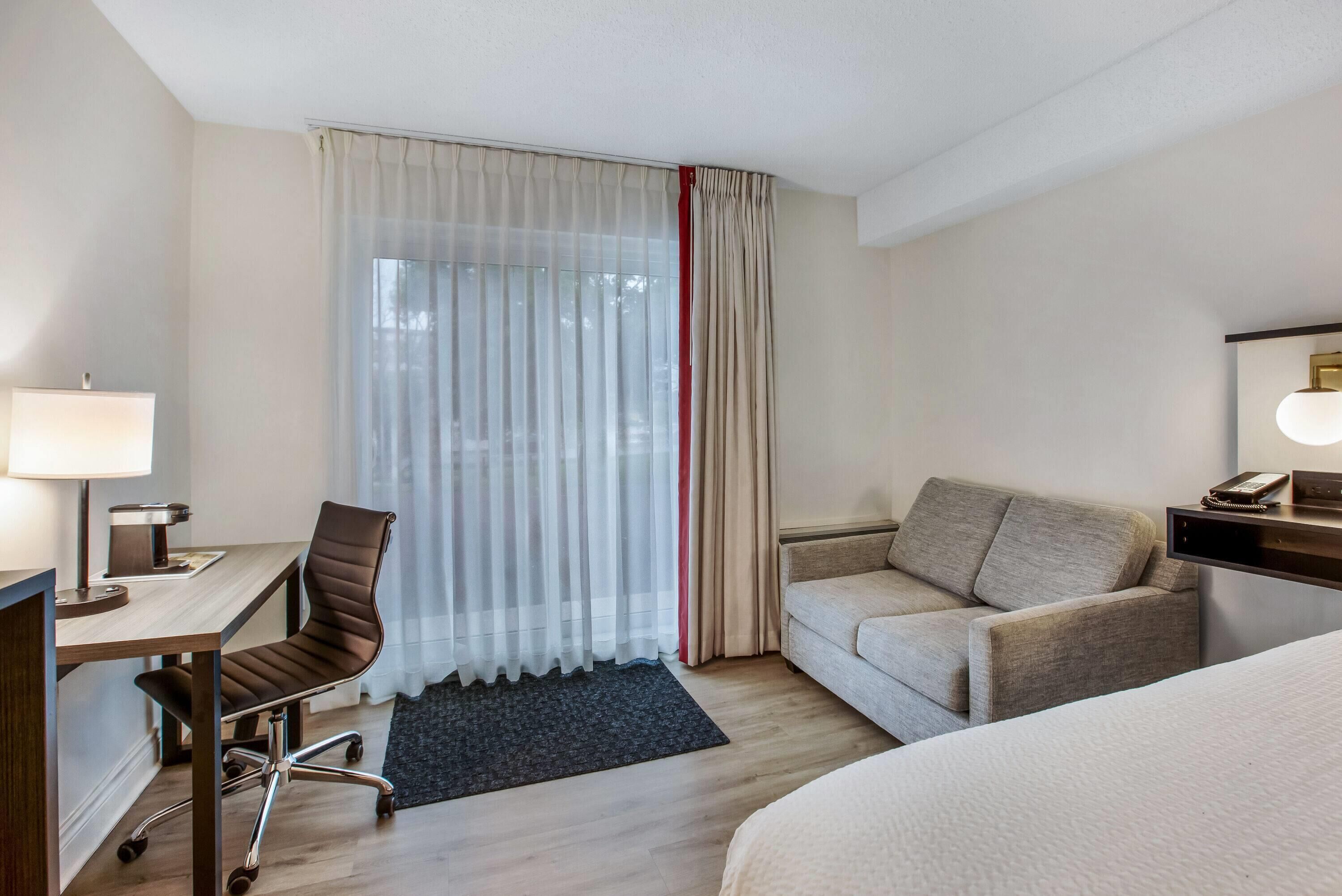 A hotel room with a desk, chair, sofa, and a bed.