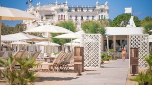 A resort with outdoor seating, umbrellas, and a large building in the background. - Grand Hotel Rimini (Rimini)