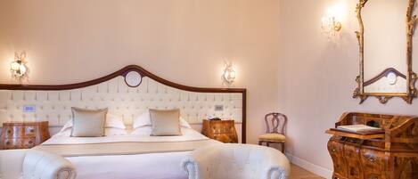 Une chambre à coucher avec un grand lit, deux fauteuils, une commode en bois et un miroir au mur.