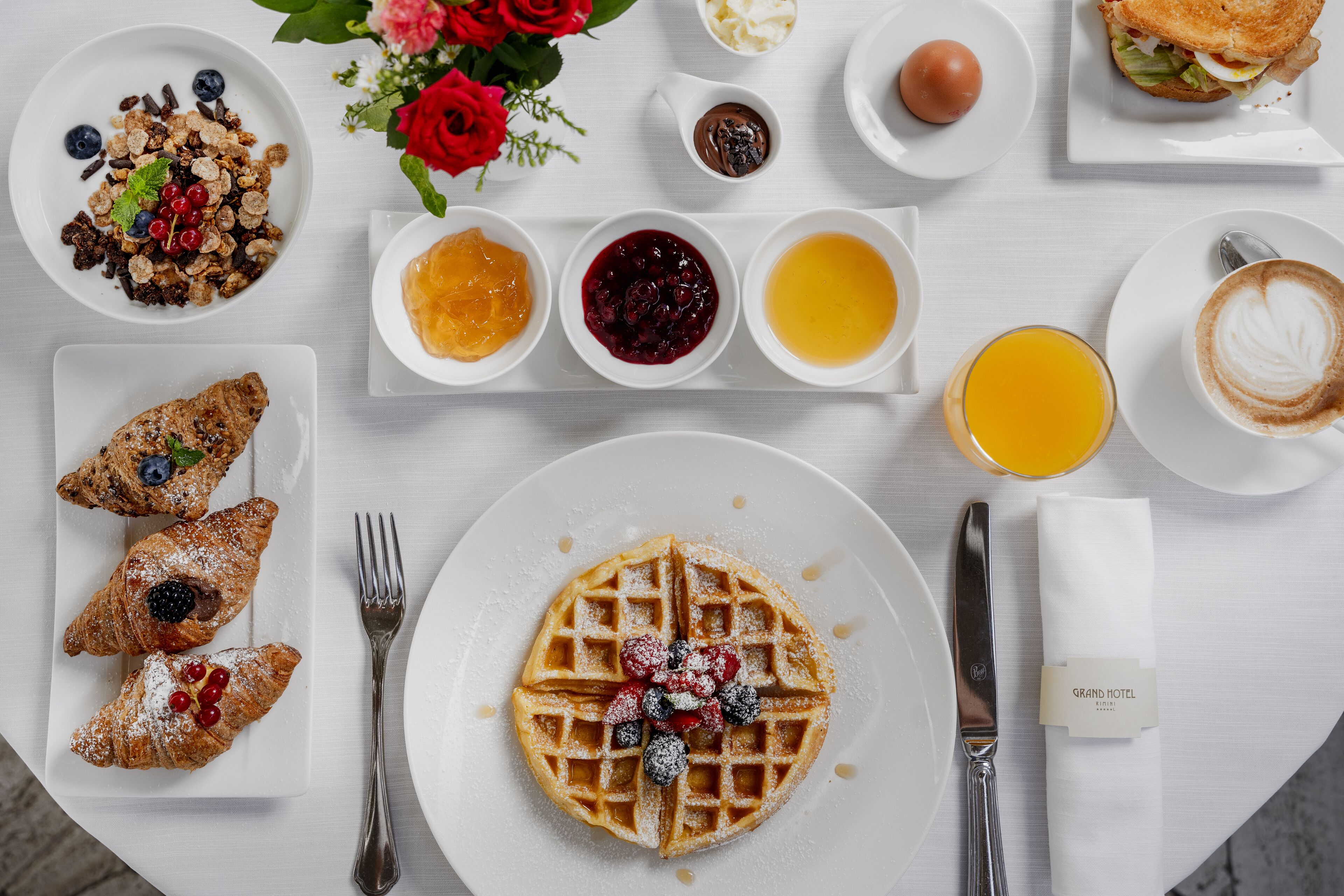 Une table dressée pour le petit-déjeuner avec des gaufres, des pâtisseries et diverses confitures présentées sur des assiettes.