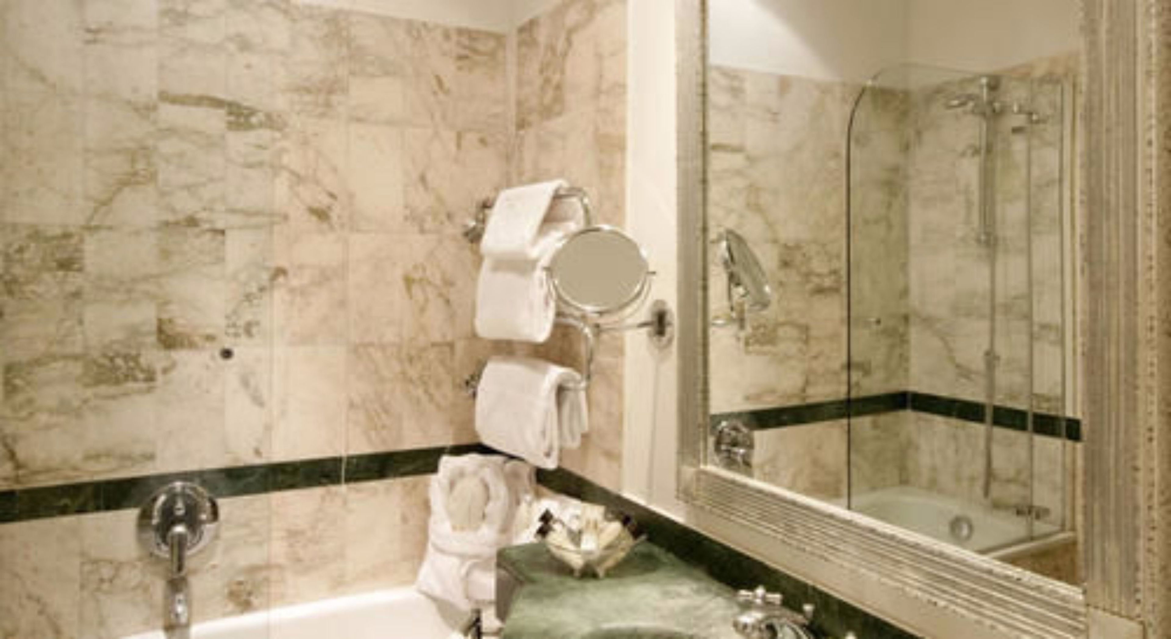 A bathroom with a marble wall, a bathtub, a sink, a mirror, and a towel rack.