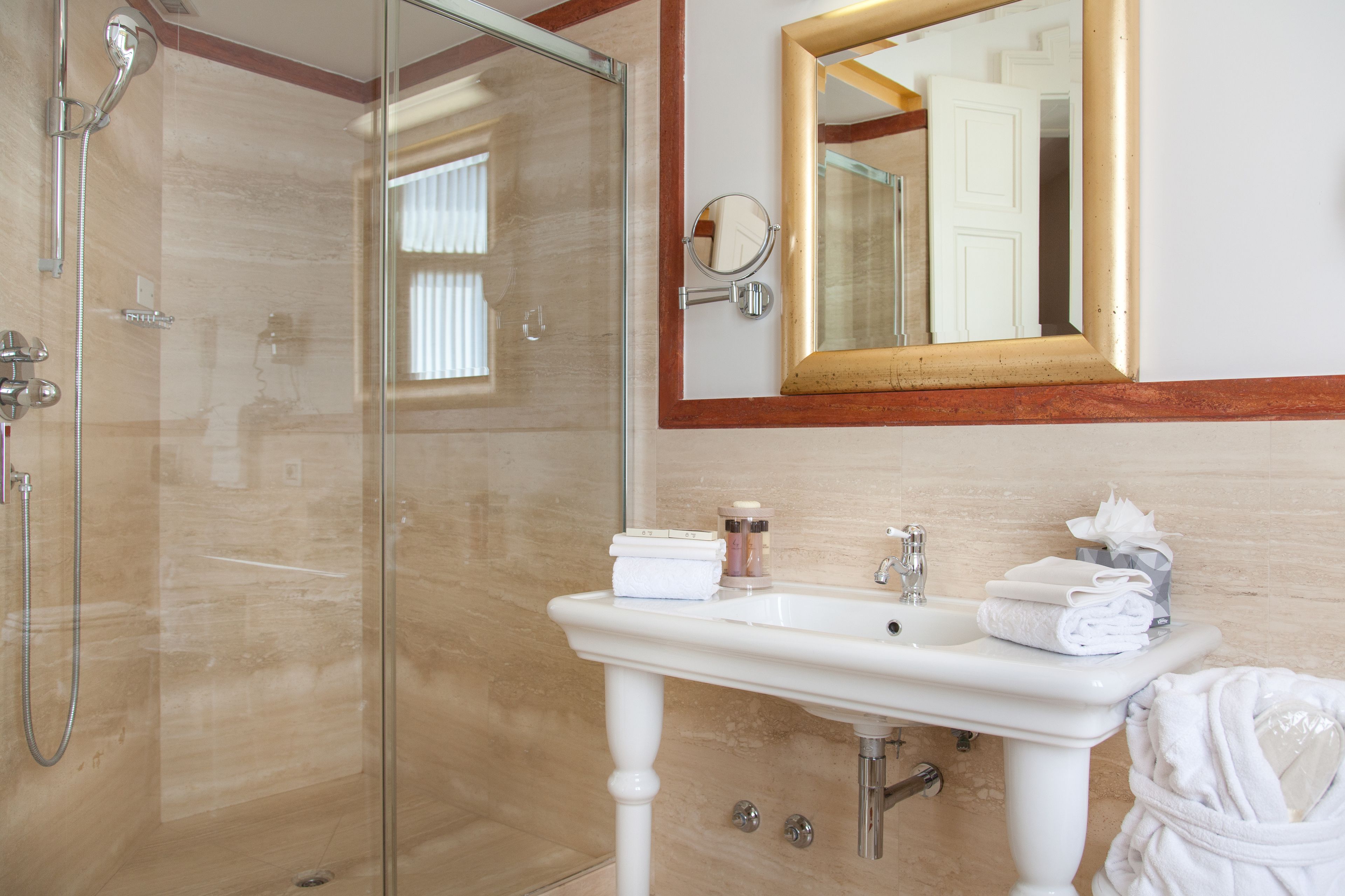 A bathroom with a glass shower enclosure, a white pedestal sink, and a mirror with a gold frame.