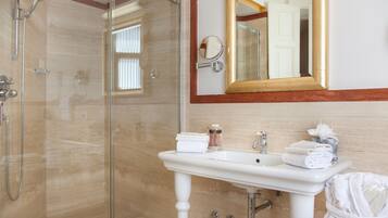 A bathroom with a glass shower enclosure, a white pedestal sink, and a mirror with a gold frame.