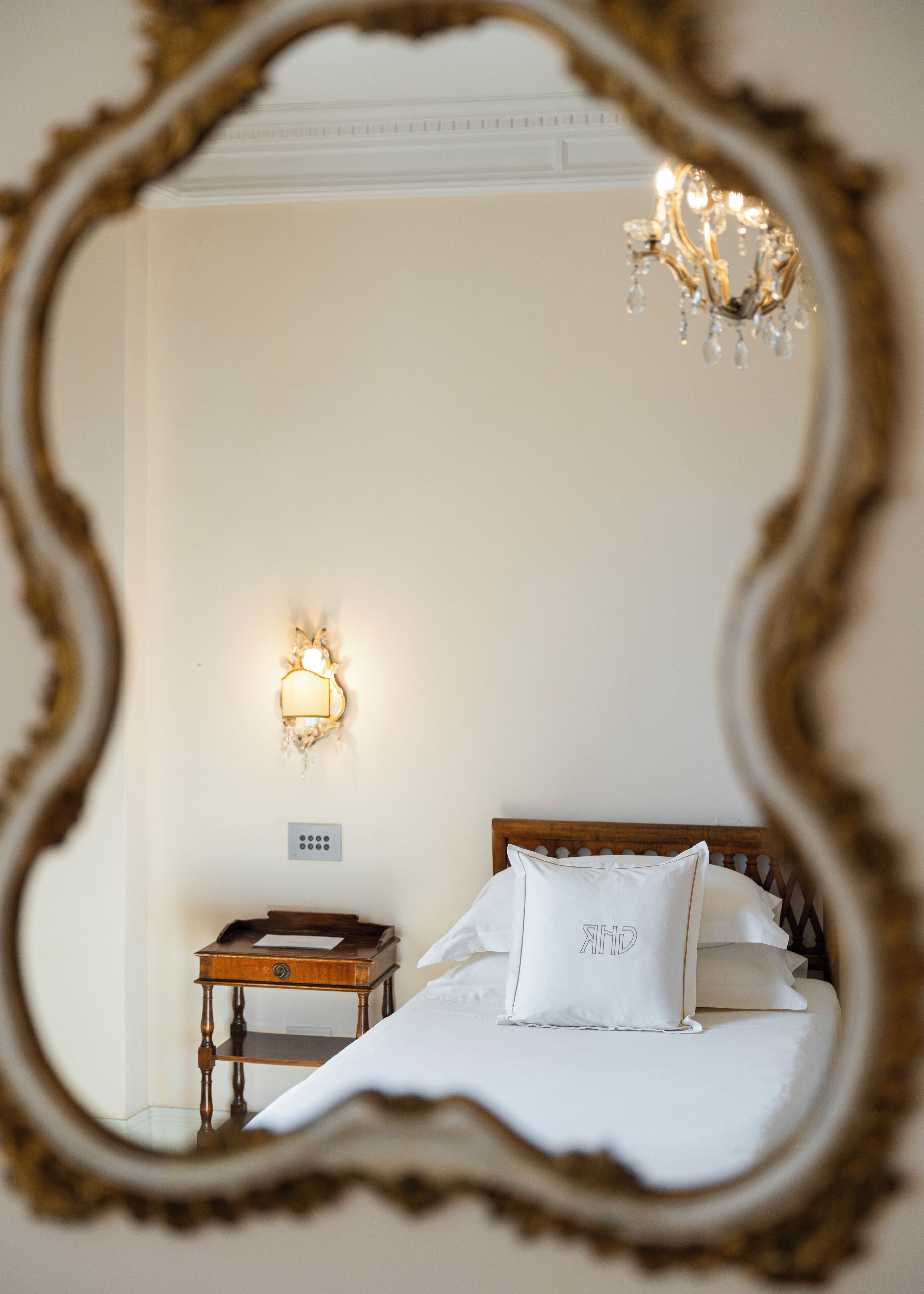 Un dormitorio con cama, mesita de noche, aplique de pared y candelabro.