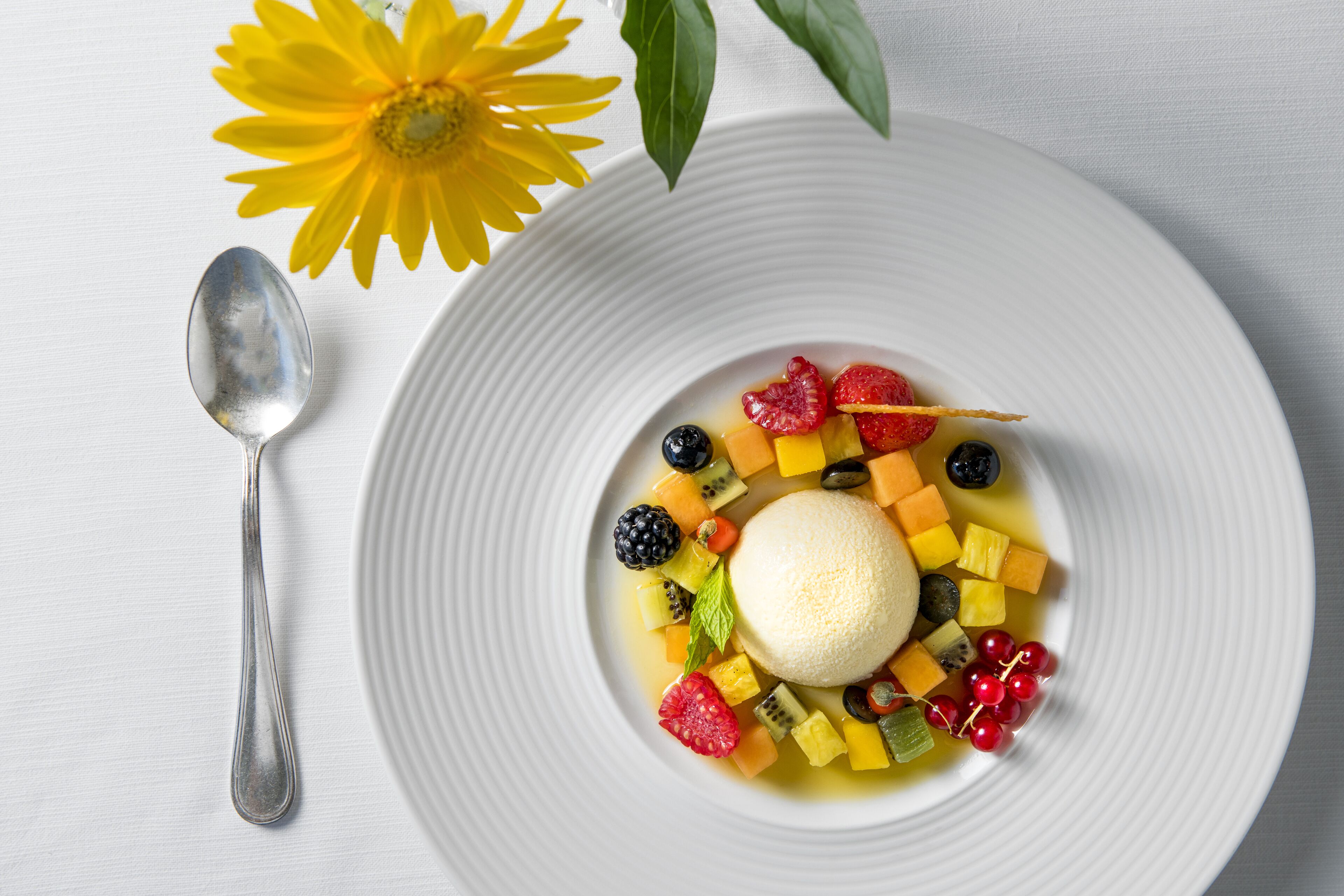 Un piatto dessert con una pallina di gelato e frutta mista.