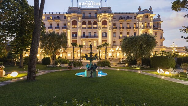 A grand hotel with a central fountain, well-maintained gardens, and a formal entrance.