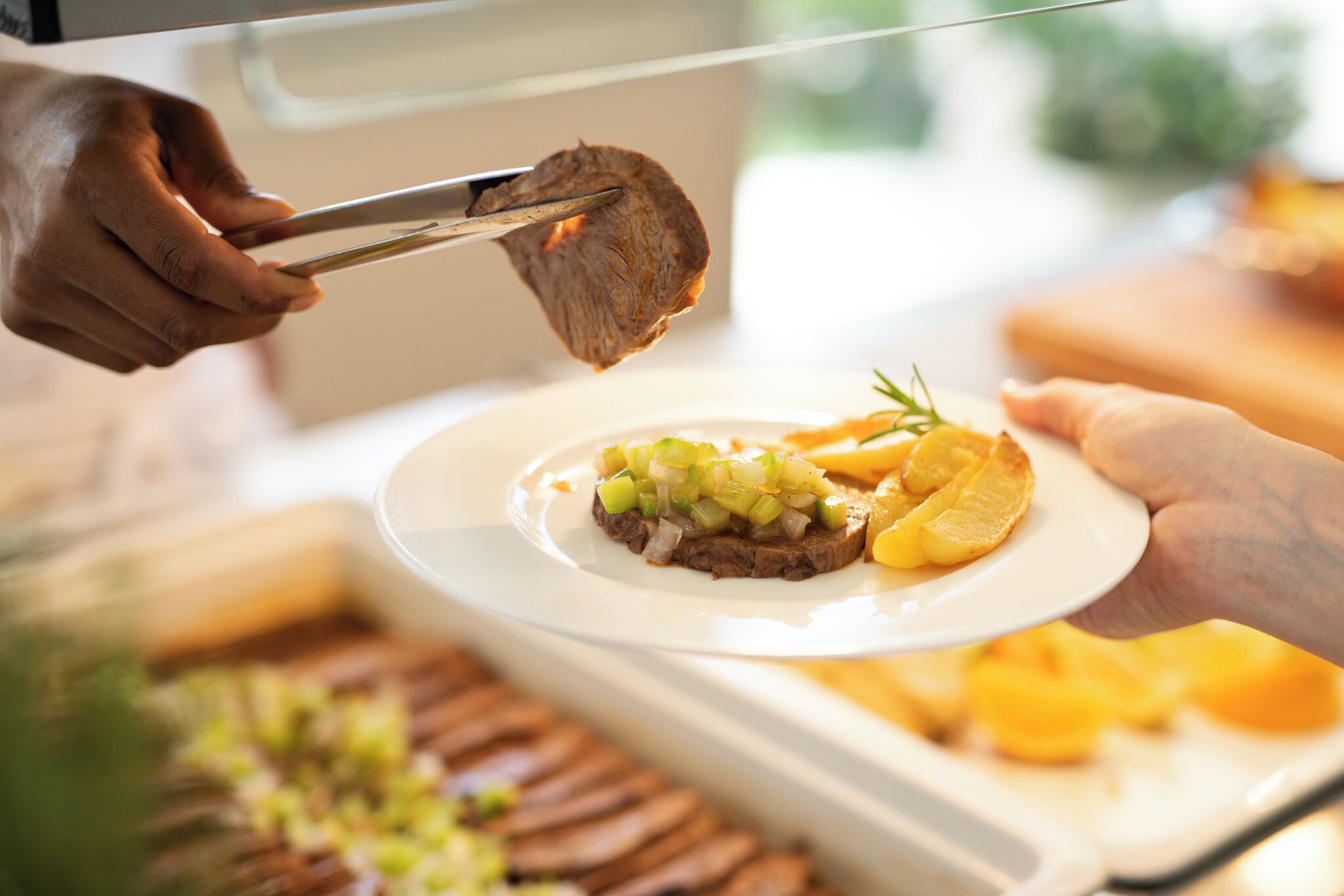 A person serving a dish with meat and vegetables on a plate.