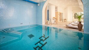 An indoor swimming pool with clear water, a tiled floor, and a lounge area with sun loungers and a potted plant.