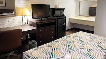 Una habitación de hotel con cama, escritorio, silla, televisión, microondas y un refrigerador pequeño.