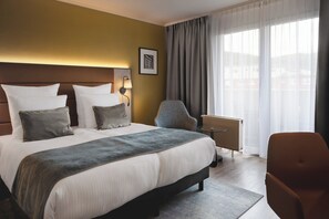 Ein Hotelzimmer mit einem großen Bett, einem Sessel, einem Heizkörper und einem Fenster mit Vorhängen.