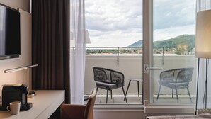 Habitación de hotel con balcón, televisión, cafetera y dos sillones.