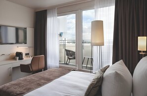 Ein Hotelzimmer mit Bett, Schreibtisch mit Kaffeemaschine, Stuhl, Fernseher und Balkon mit Aussicht.