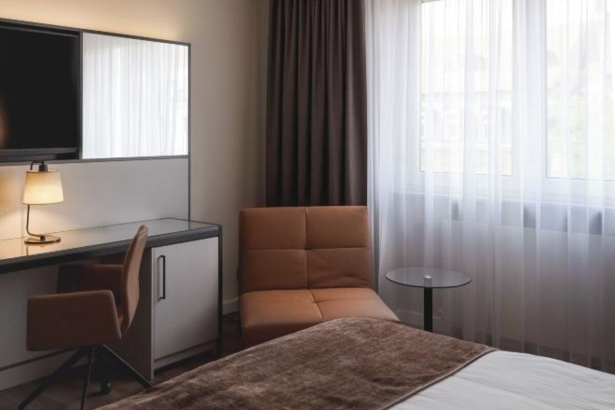 Habitación de hotel con cama, escritorio, silla, televisión y una pequeña mesa.