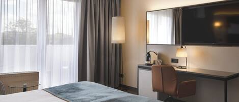 A hotel room with a bed, a desk, a chair, a television, and a window with curtains.