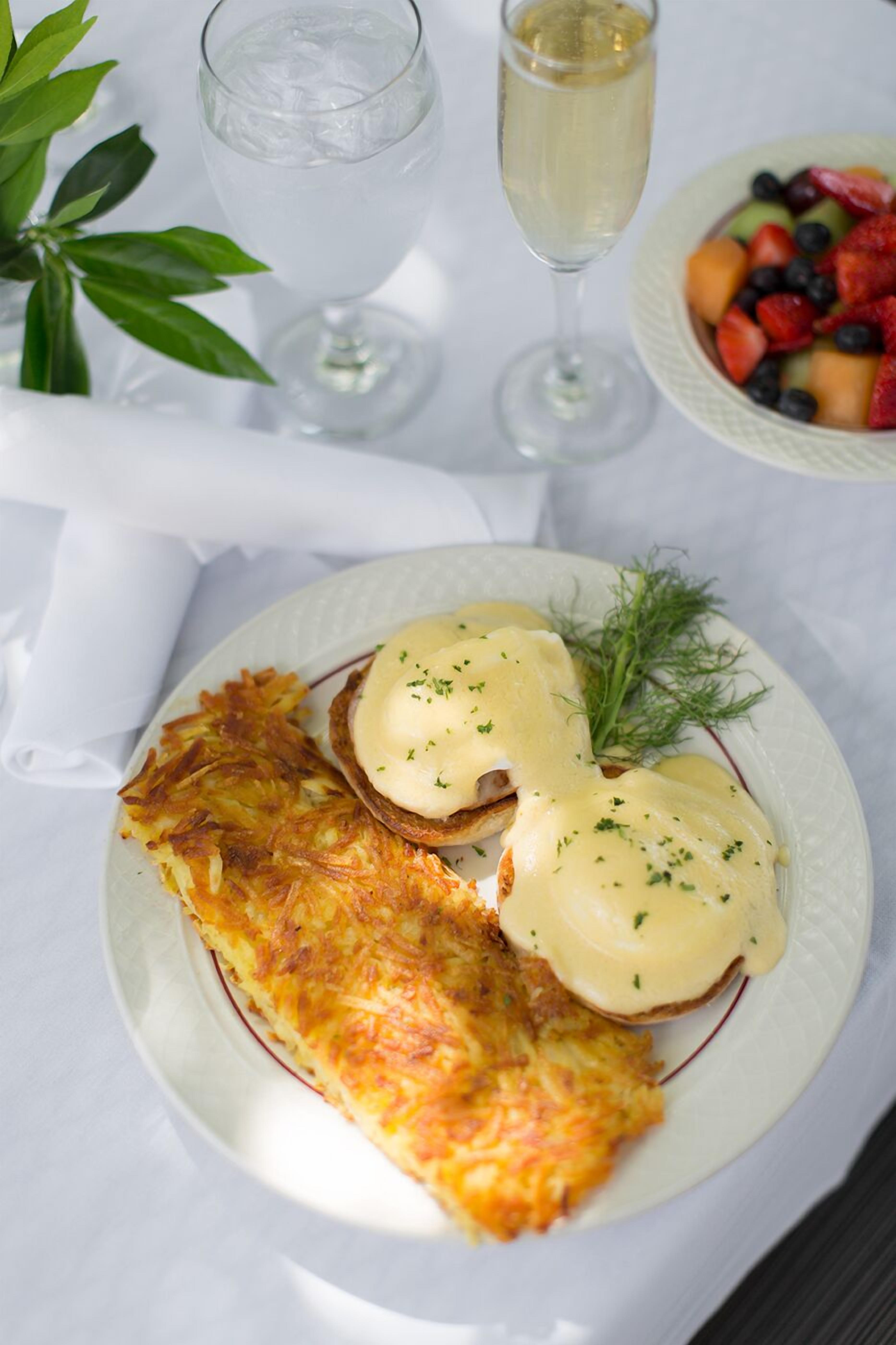 En tallrik med ägg benedict, ett glas vatten och en skål med frukt.
