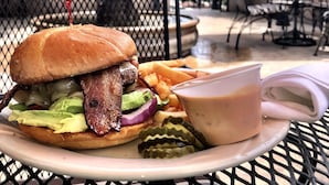 A meal consisting of a burger, fries, and a drink on a table with a metal fence and chairs in the background. - Red Lion Hotel Rogue Regency Medford Airport (Medford)