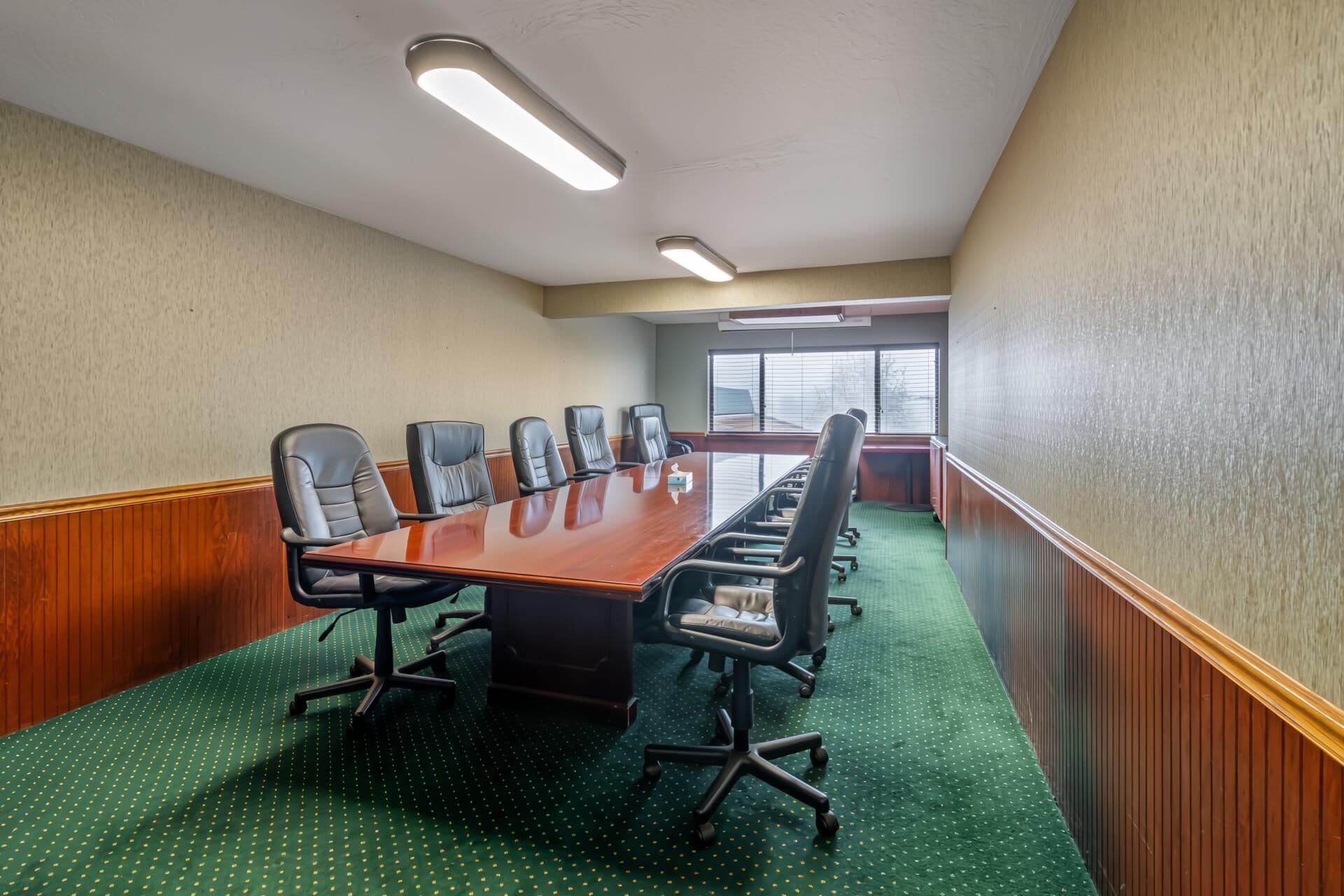 A conference room with a long table, chairs, and a carpeted floor.
