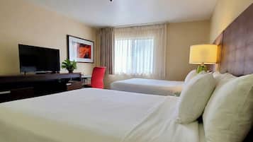Habitación de hotel con una cama grande, un escritorio con televisor, una silla, una ventana con cortinas y una lámpara.