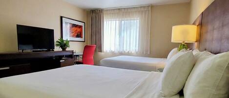 A hotel room with a large bed, a desk with a TV, a chair, a window with curtains, and a lamp.