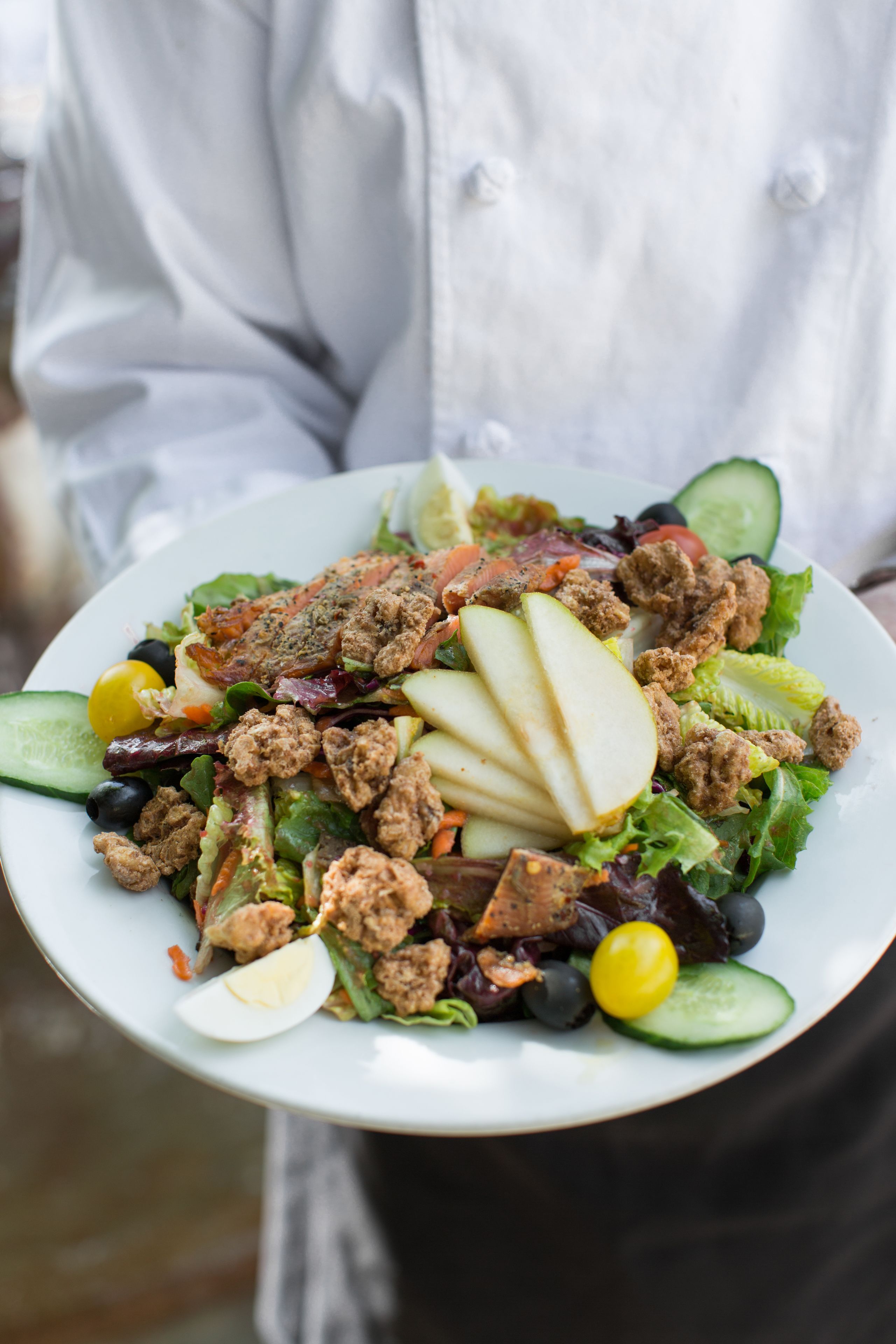 A plate of salad with various ingredients including lettuce, tomatoes, cucumbers, and sliced apples.